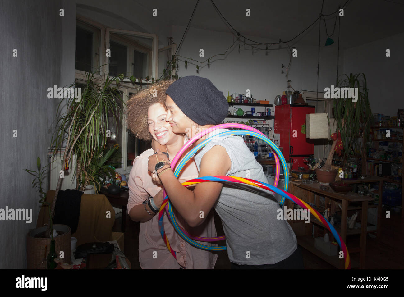 Uomo che abbraccia la ragazza sorridente mentre tiene i cerchi di plastica a casa Foto Stock