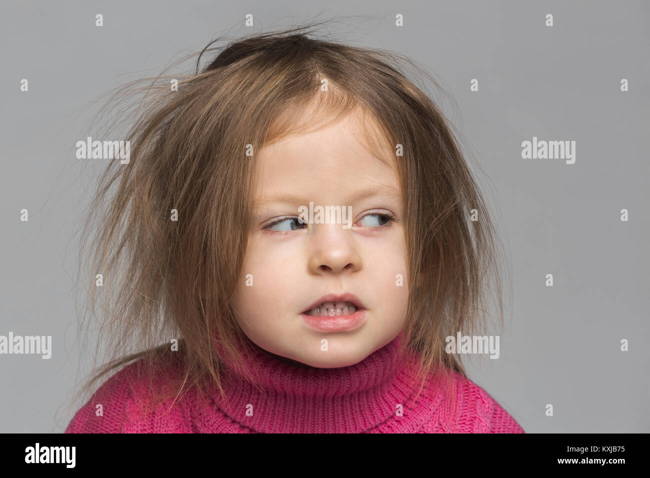 Primo piano di cute ragazza con i capelli disordinati guardando via contro sfondo grigio Foto Stock