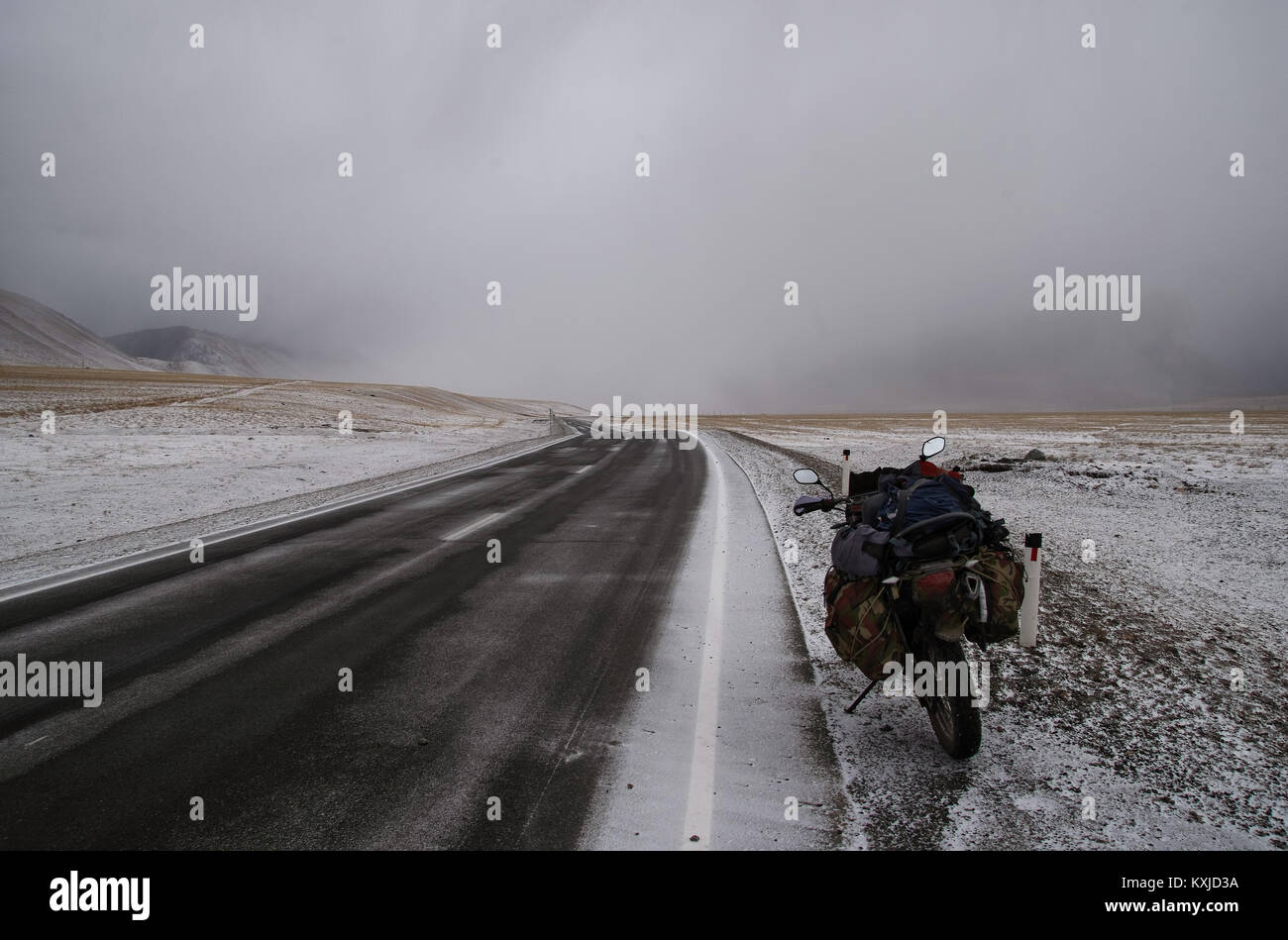 Motociclo traveler su asfalto stradale percorso su una neve invernale deserto montagna selvaggia valle sotto una drammatica storm cloud tratto Chuysky montagne di Altai Siber Foto Stock