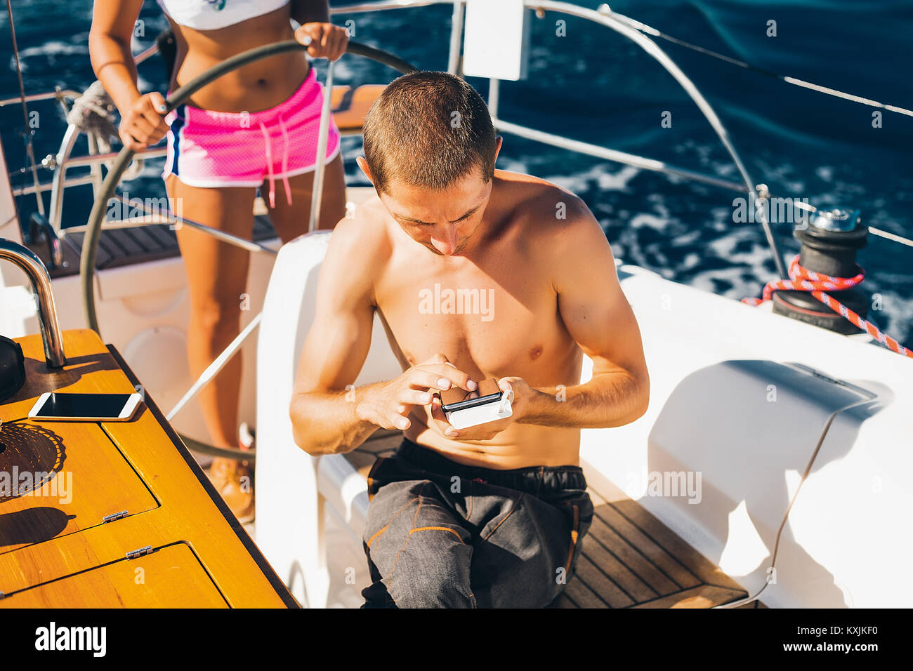 Donna in bikini barca sterzo, uomo in primo piano utilizza lo smartphone Foto Stock