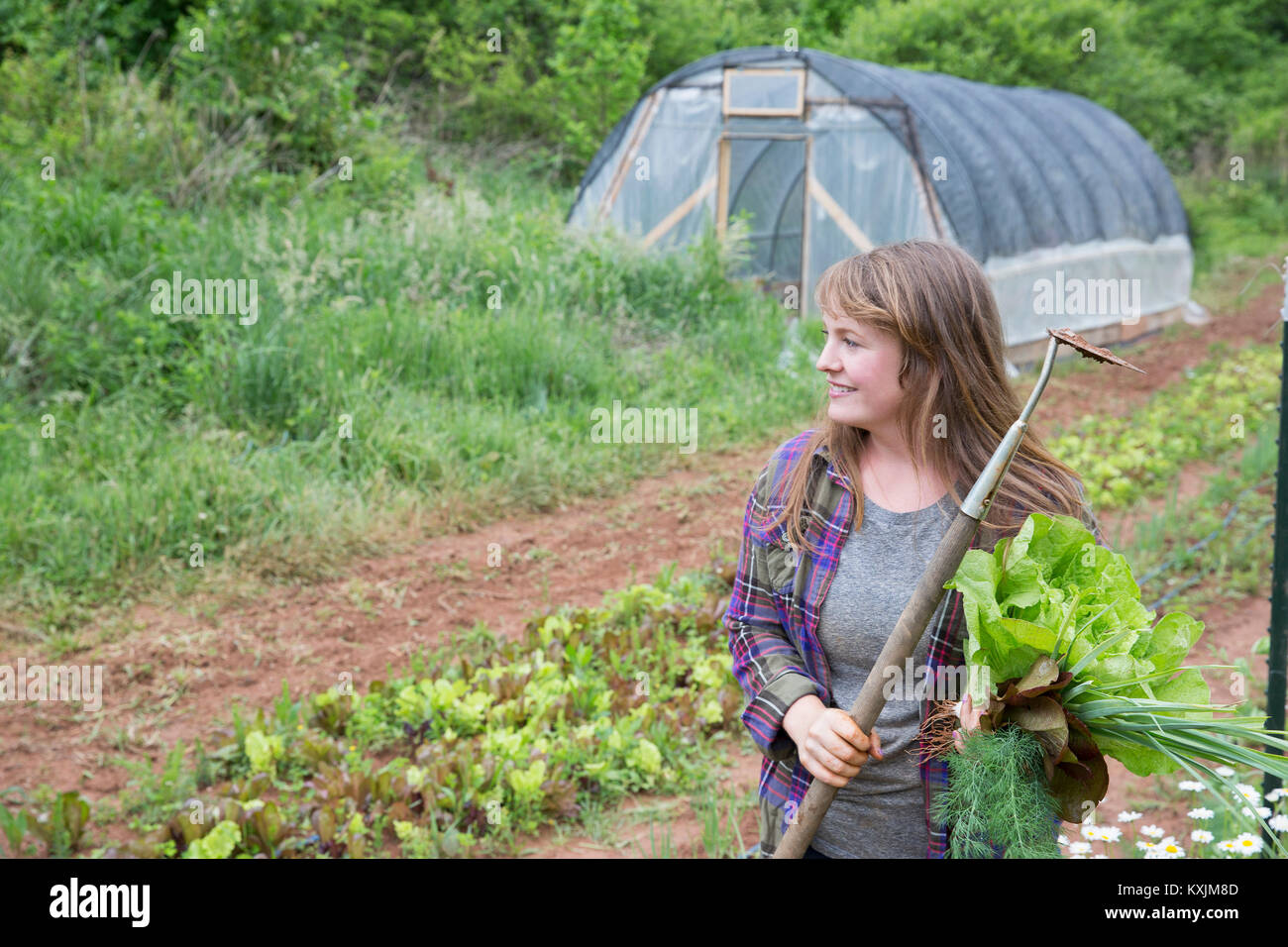 Donna con la zappa in un orto che guarda lontano sorridente Foto Stock