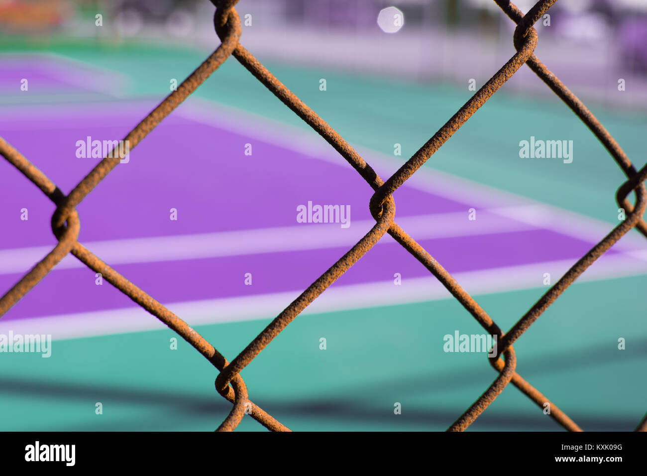 Close up di rosso rusty catena collegamento recinto contro il viola e il verde menta campo da tennis Foto Stock