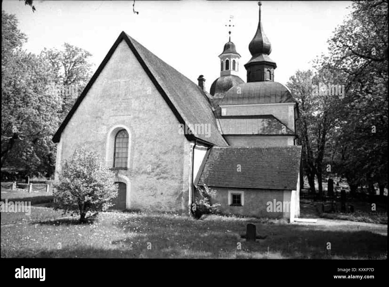 Vista della chiesa di Bälinge circondata da alberi, che mostra le sue pareti in pietra medievale dipinte di bianco e il tetto con tegole rosse. Foto Stock