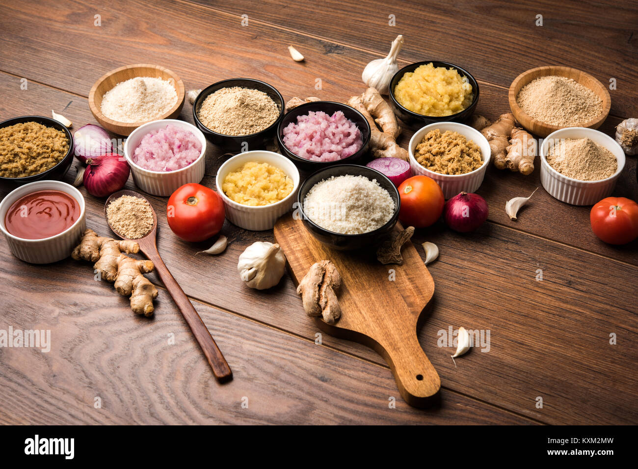 Lo zenzero, aglio, la cipolla e il concentrato di pomodoro e polvere e in forma grezza. Un gruppo di Indiani di base degli ingredienti alimentari su sfondo di legno. Messa a fuoco selettiva Foto Stock