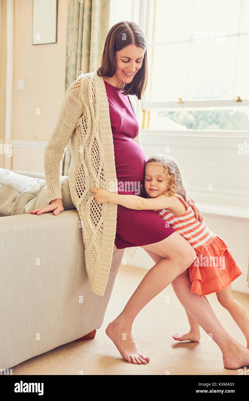 Ragazza ascoltando e abbracciando in stato di gravidanza della madre stomaco Foto Stock
