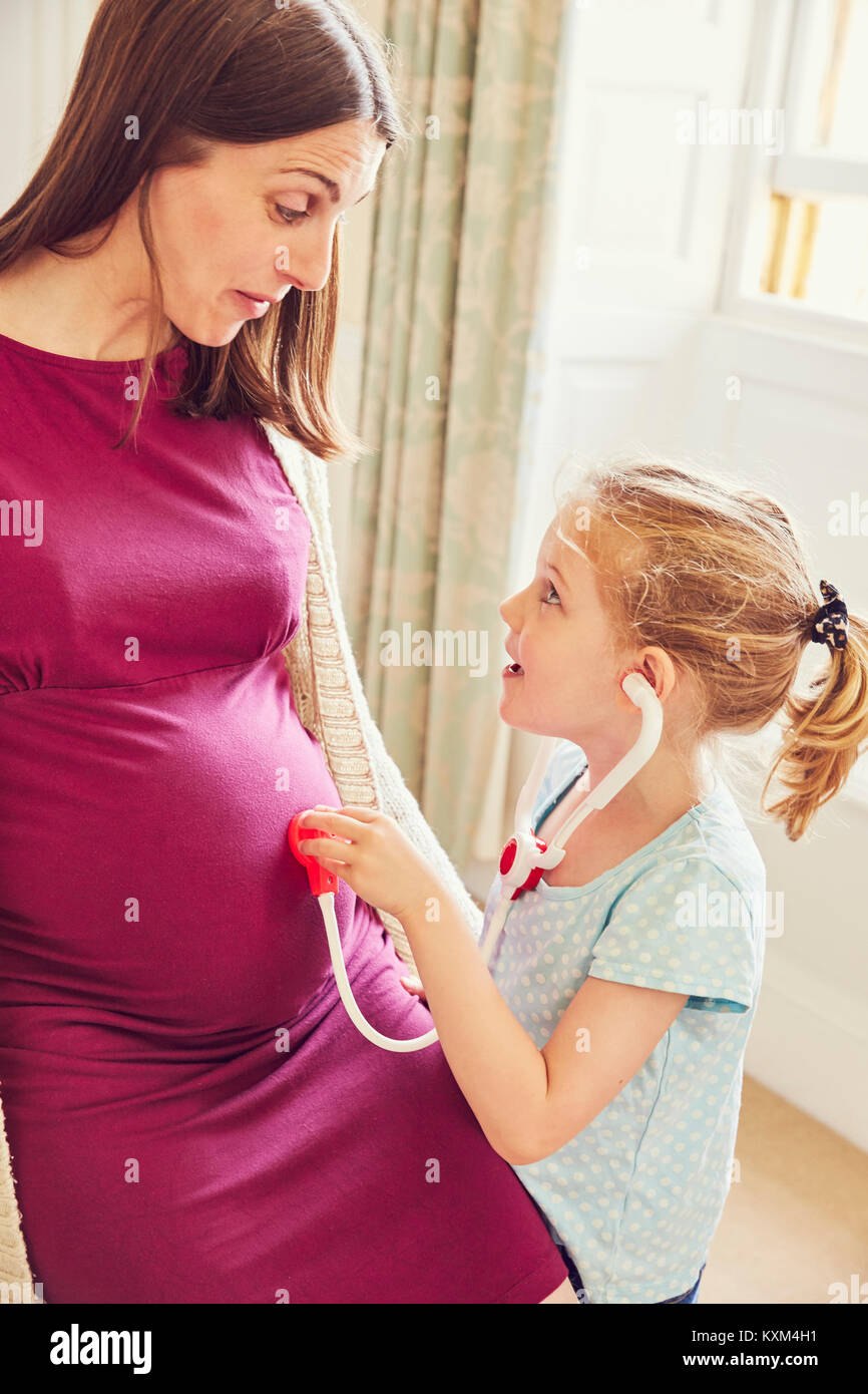 Ragazza con stetoscopio giocattolo ascolto a donne in stato di gravidanza della madre stomaco Foto Stock