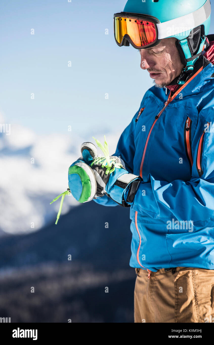 Uomo maturo indossando skiwear,mettendo su guanti da sci Foto Stock