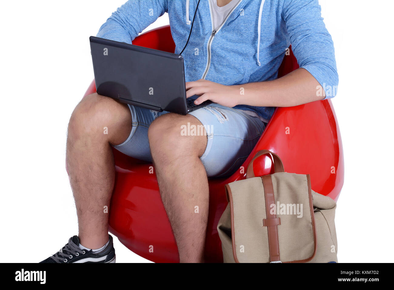 Chiusura del giovane uomo seduto in rosso pouf utilizzando laptop con lo zaino. Il concetto di istruzione Foto Stock