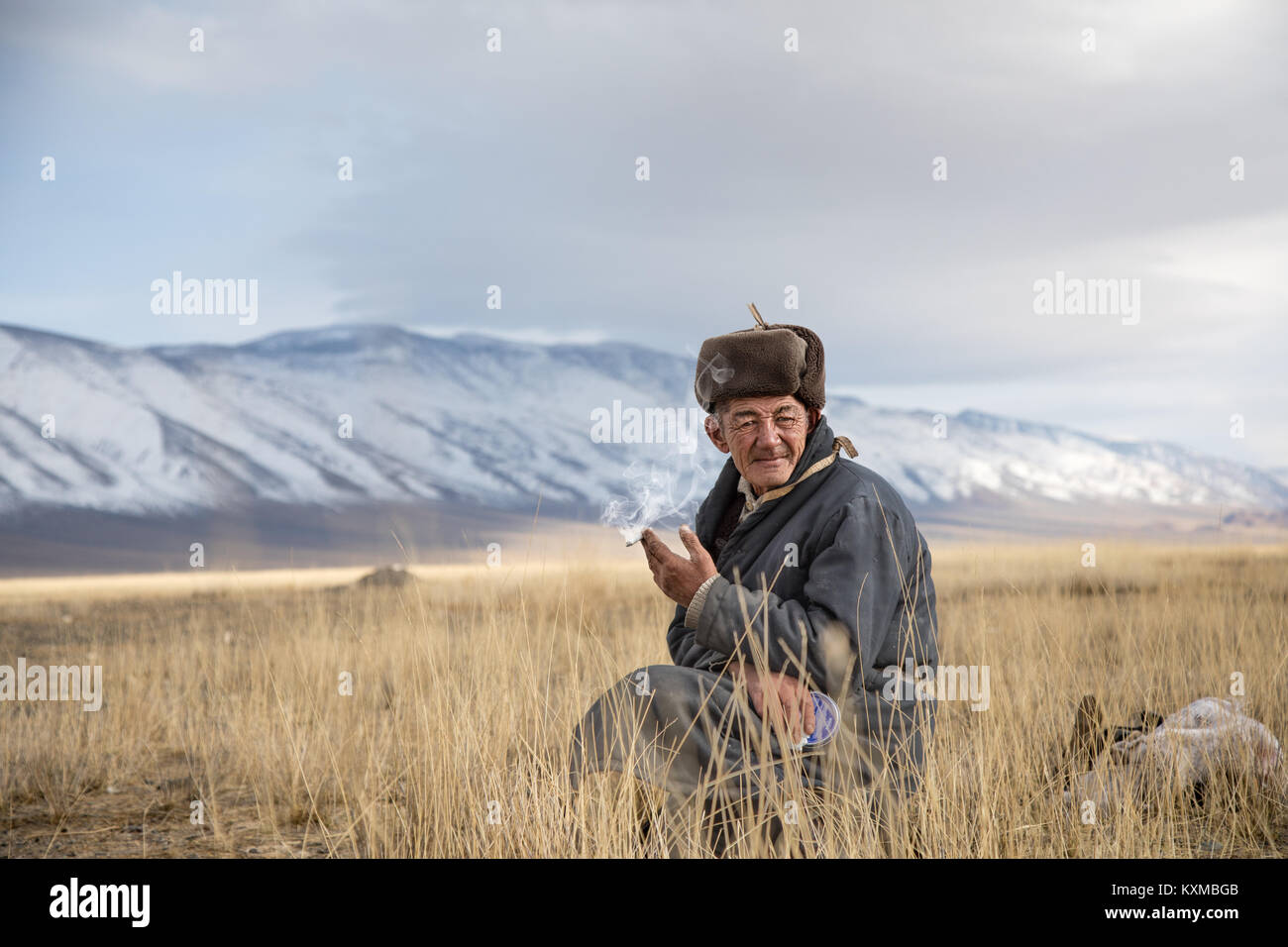 Il mongolo paese rurale lato vecchio Sigaretta fumare cappello di pelliccia Mongolia nonno appoggio posti a sedere Foto Stock