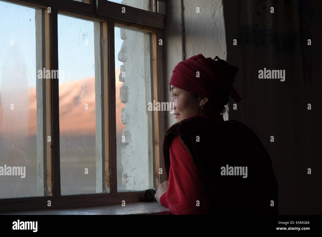 Il mongolo paese rurale lato il kazako giovane ragazza guardando fuori dalla finestra tramonto inverno in Mongolia Foto Stock