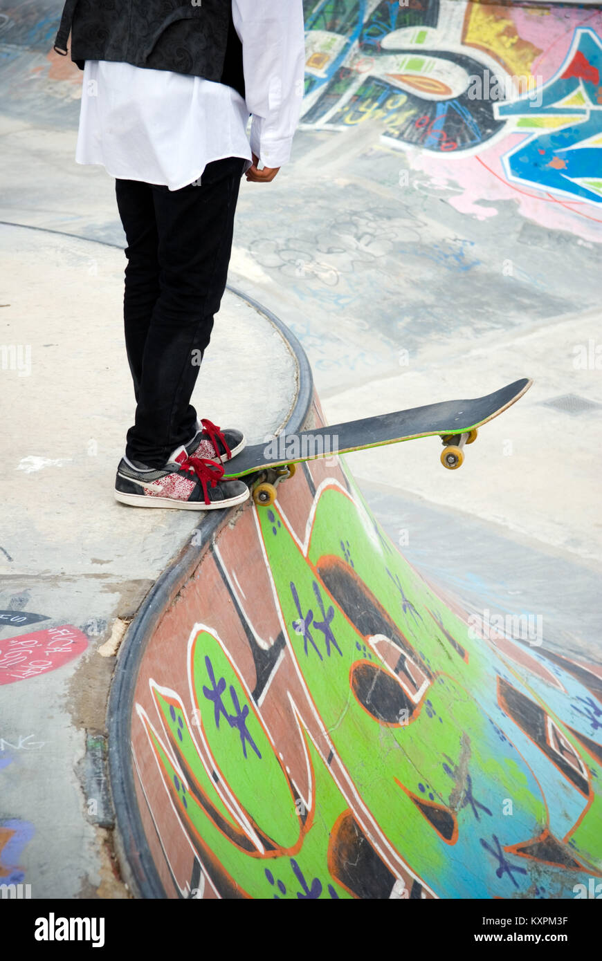 Raccolto di tredici anni di bilanciamento del maschio il suo skateboard sul bordo di un pendio a skate park coperto di graffiti Foto Stock