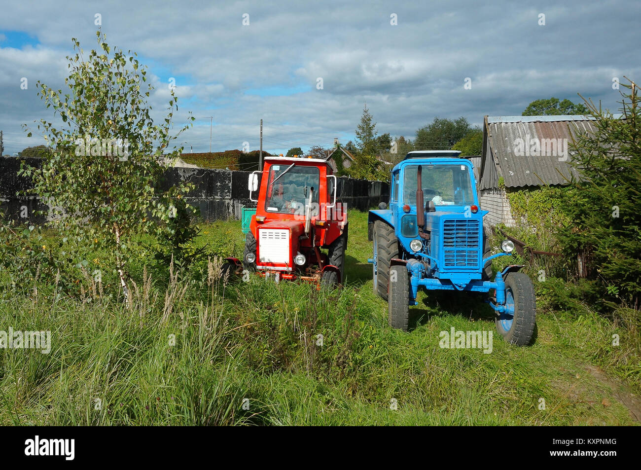 Il rosso e il blu trattore sono in cantiere, due trattori in un villaggio vicino alla casa in legno Foto Stock