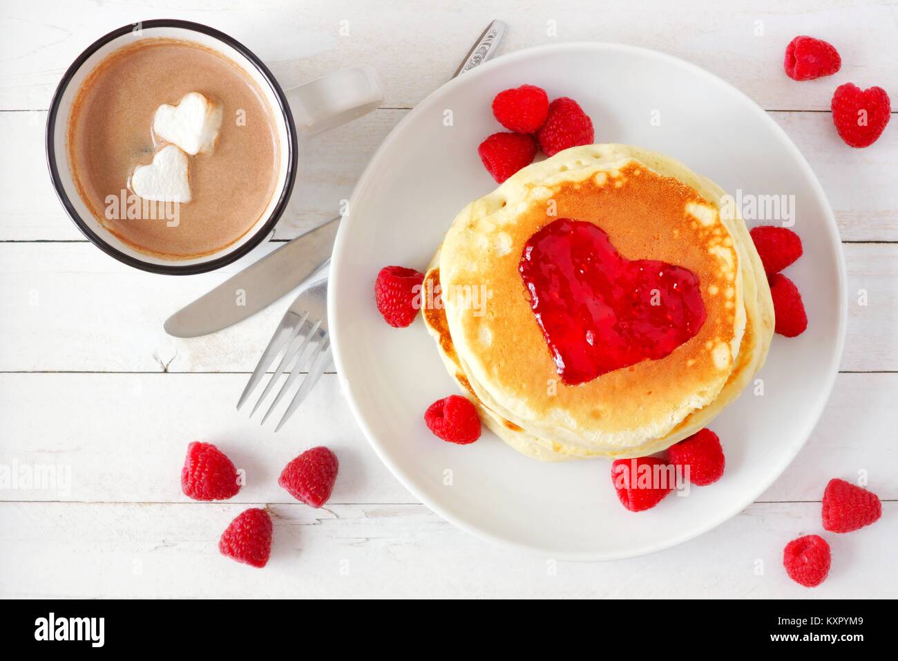 Frittelle con marmellata a forma di cuore e la cioccolata calda con marshmallow cuori su un bianco tavola di legno. Il concetto di amore. Foto Stock