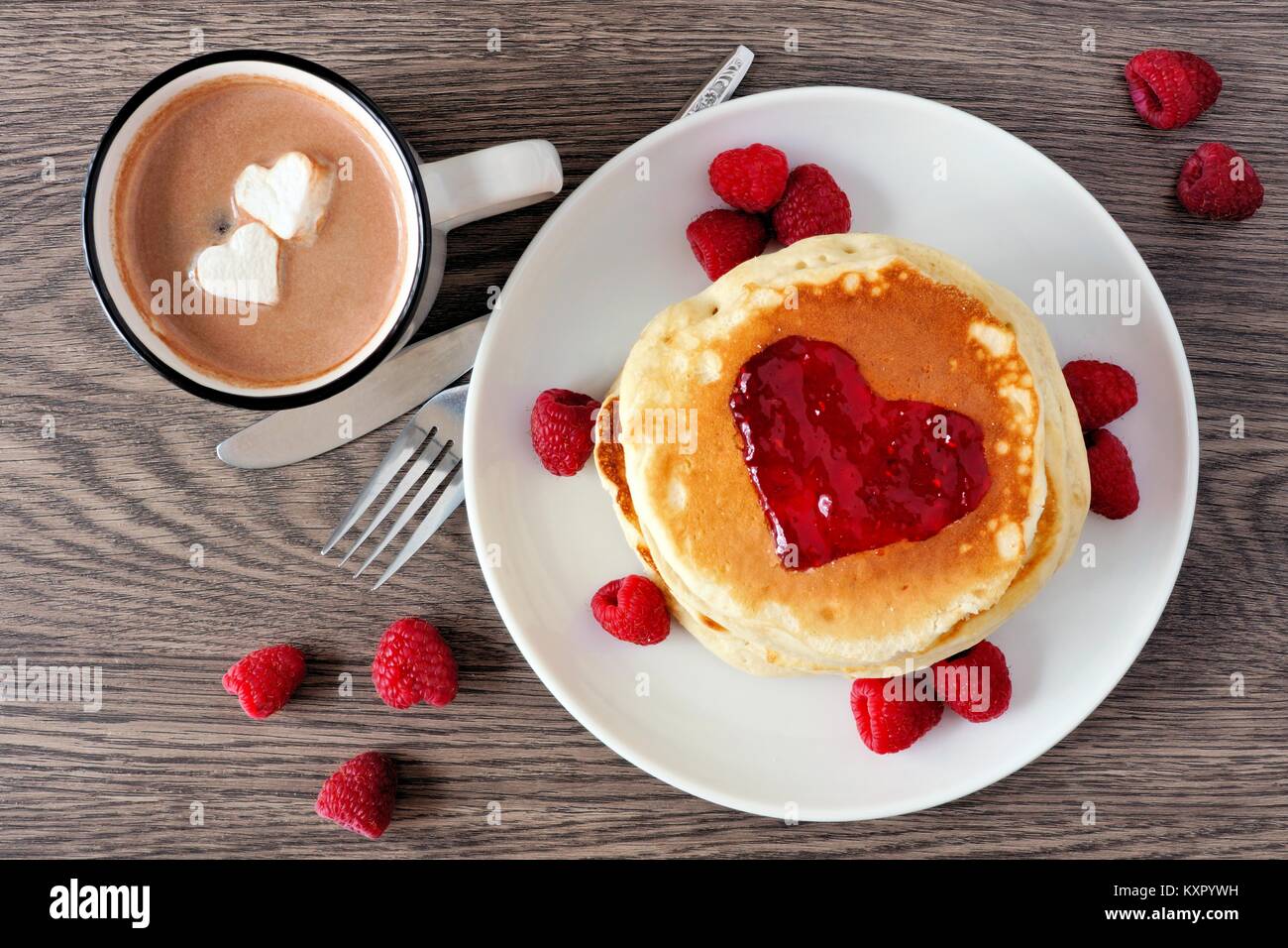 Frittelle con marmellata a forma di cuore, cioccolato e lamponi su uno sfondo di legno. Il concetto di amore. Foto Stock