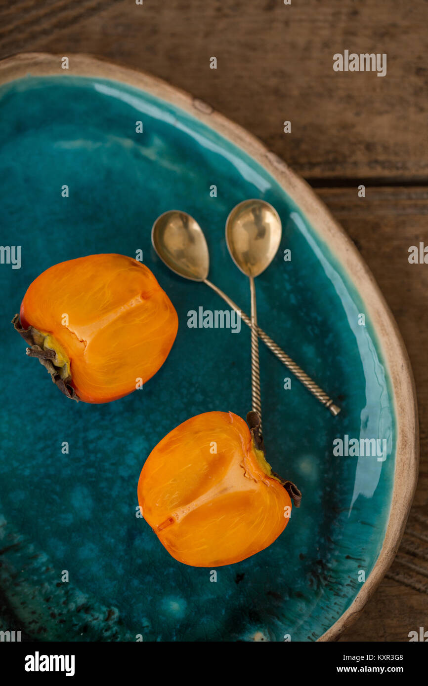 Deliziosa persimmon tagliato a metà collocati in ceramica color turchese la piastra al di sopra del piano portapaziente rustico. Vista dall'alto. Foto Stock