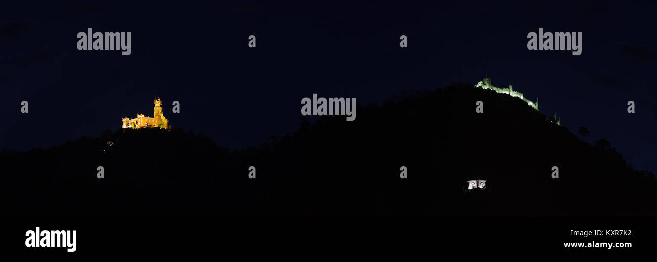Pena Palace (Palacio da Pena) e Mori Castello (Castelo dos Mouros) accesa contro un blu scuro cielo notturno sulla sommità di Sintra dark montagne. Lis Foto Stock