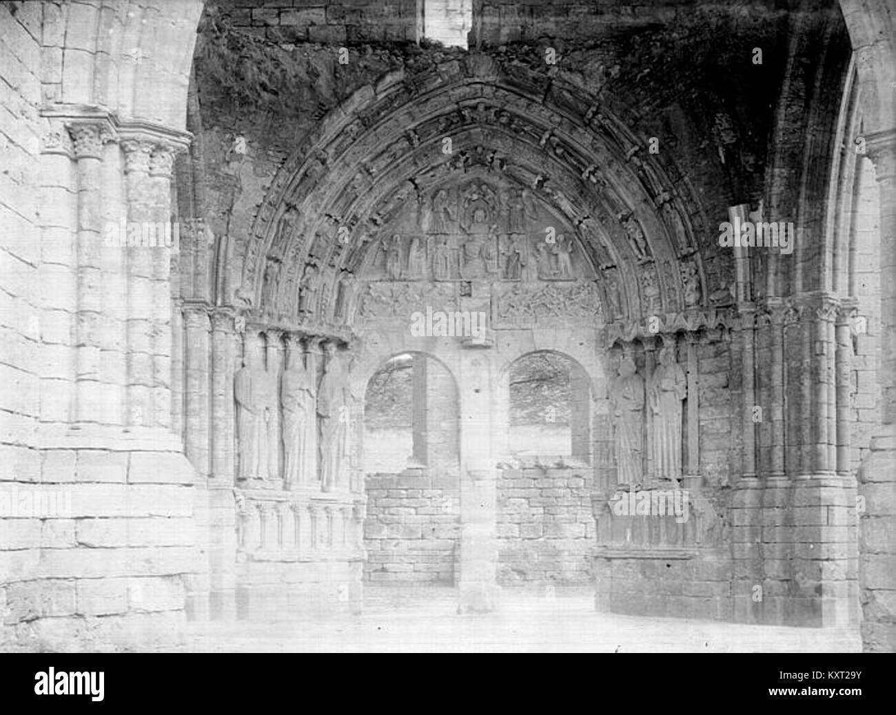 Fotografia che mostra il portale principale della chiesa di Larchant, in Francia. L'immagine si concentra sull'ingresso in pietra scolpita e su elementi gotici decorativi documentati dalla Médiathèque de l'Architecture et du patrimoine. Foto Stock