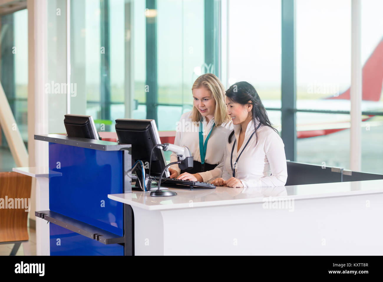 Receptionist multietnica tramite il computer al banco in aeroporto Foto Stock