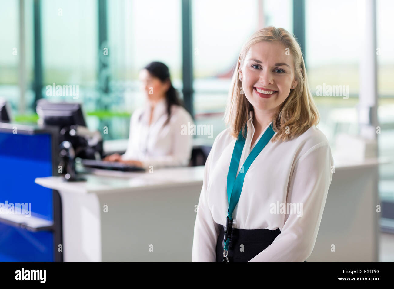 Ritratto di giovane personale di terra sorridere mentre collega di lavoro presso la reception in aeroporto Foto Stock