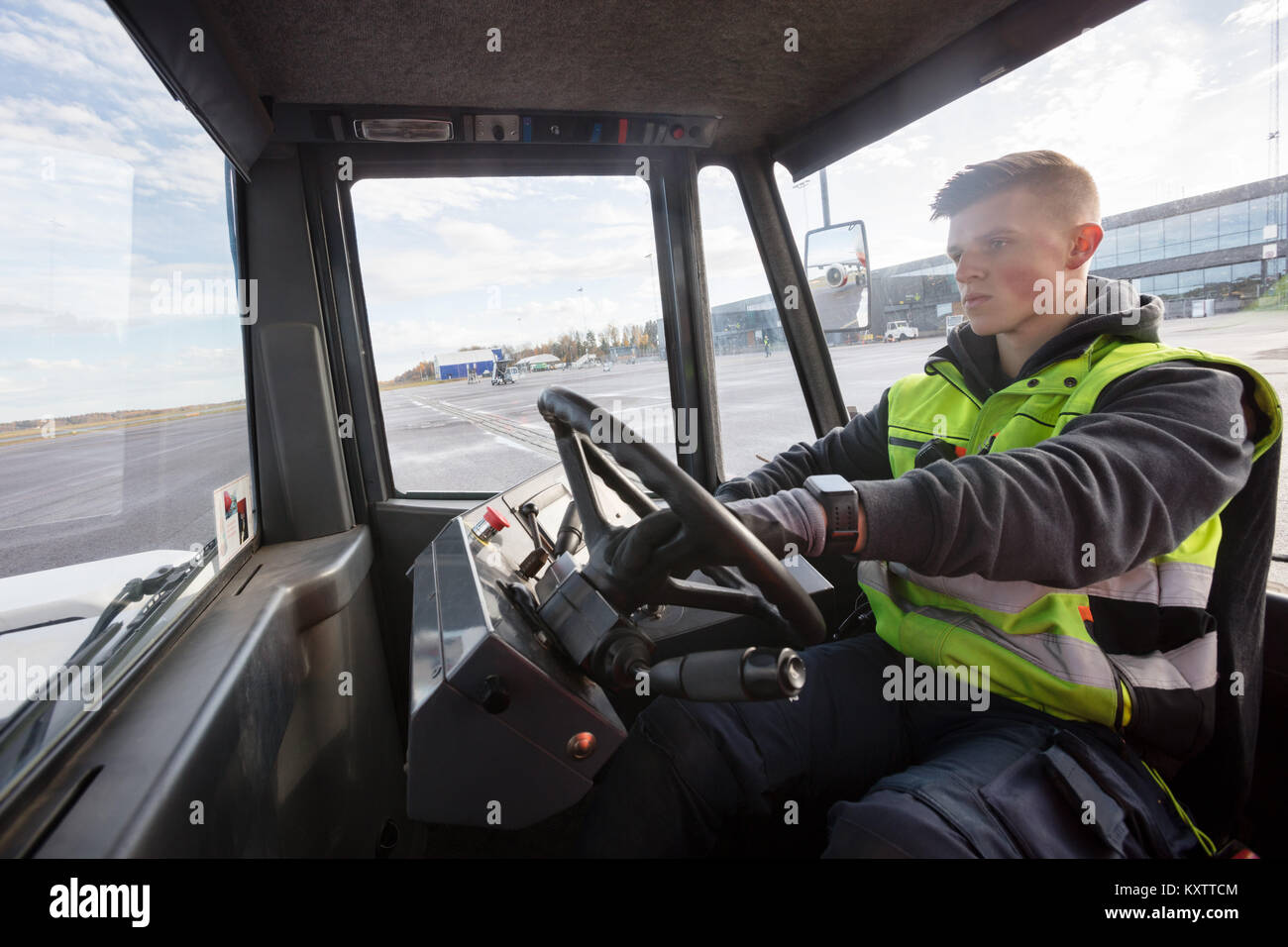 Lavoratore di sesso maschile di guida carrello di traino sulla pista in aeroporto Foto Stock