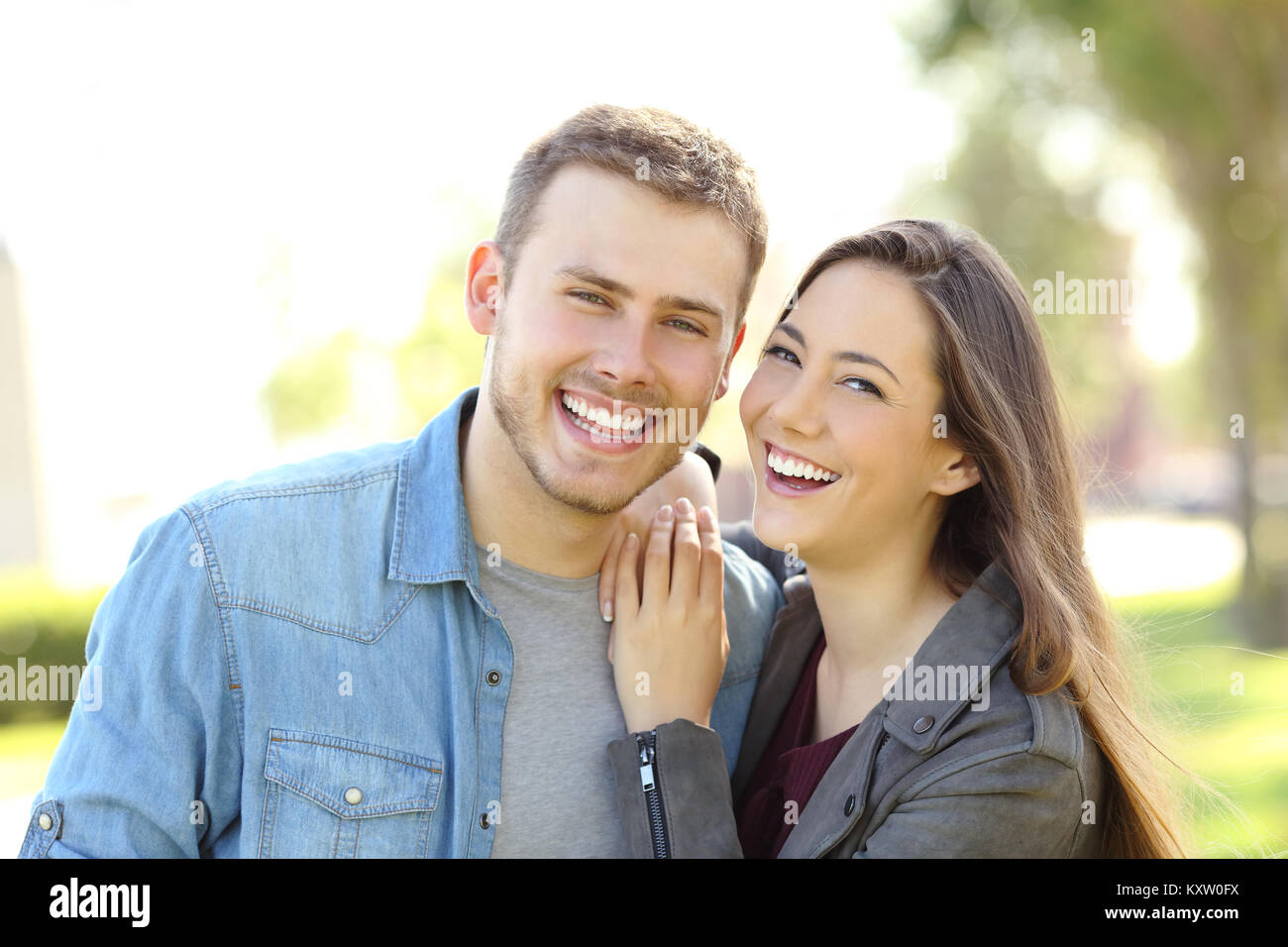 Vista frontale di un paio di posa all'aperto sorridente e guardando a voi in un parco con uno sfondo verde Foto Stock