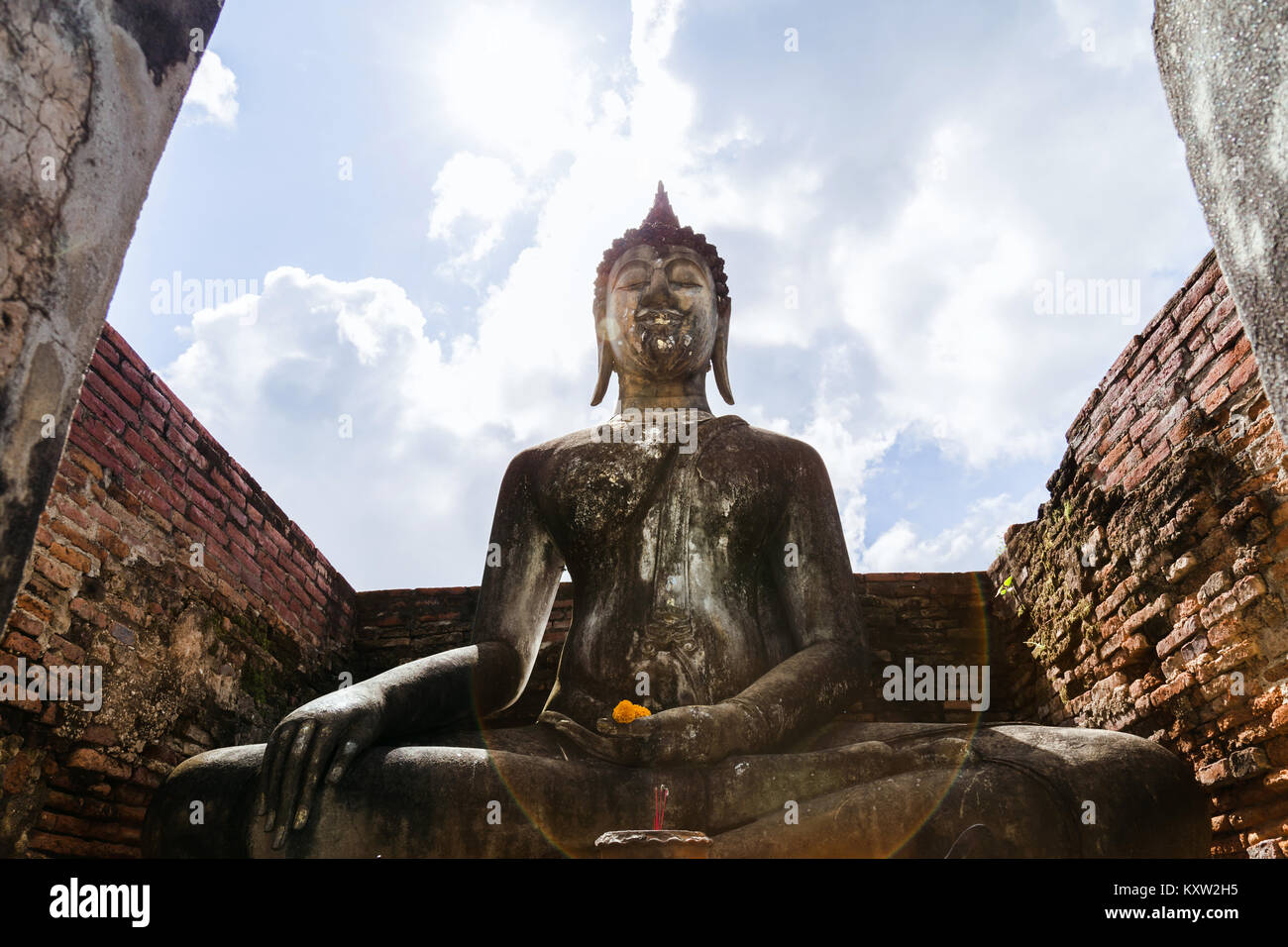 Un atteggiamento di soggiogare Mara buddha con lens flare light blue sky background a Wat Sri Chum tempio di Sukhothai Historical Park, Thailandia. Foto Stock