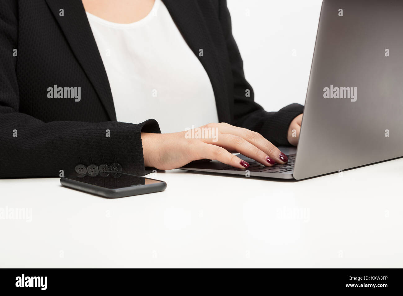 Mani di una giovane donna digitando su un computer portatile in una vista ravvicinata con un telefono cellulare a fianco Foto Stock