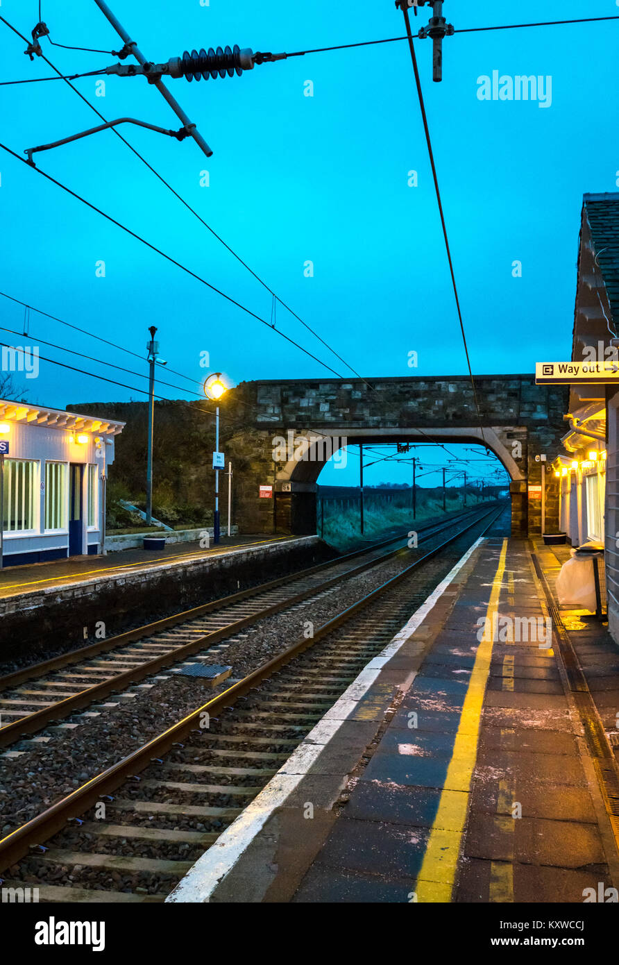 Drem stazione ferroviaria, East Lothian, Scozia, al tramonto con le luci accese e la via di uscita segno illuminato Foto Stock