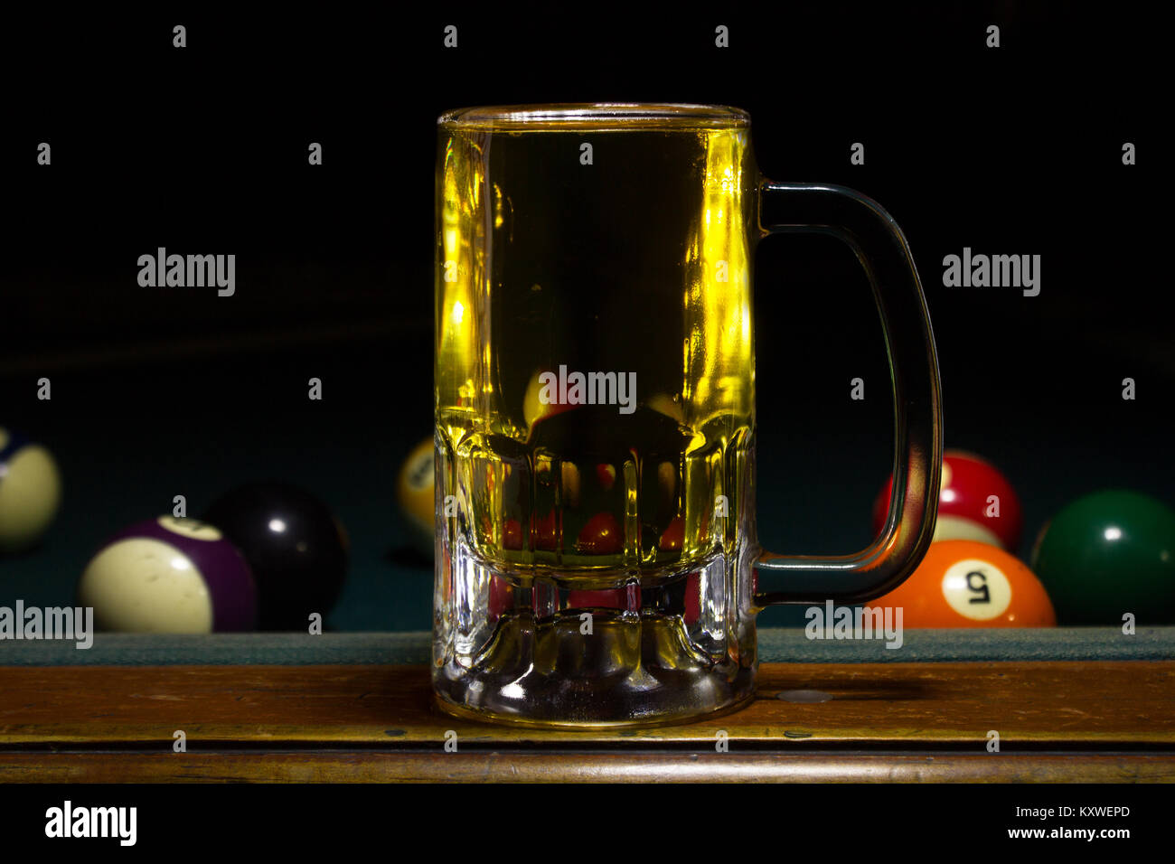 Una tazza a freddo con una birra su di un tavolo da biliardo con sfondo nero Foto Stock