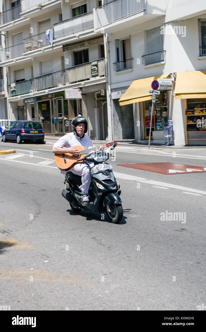 Uomo che cavalca scooter giù per la collina e di suonare una chitarra a Nizza Francia Foto Stock