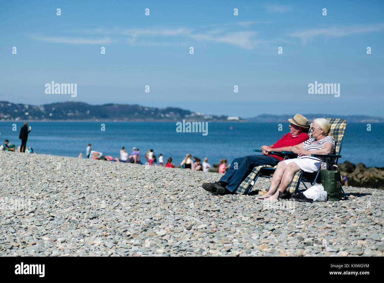 Coppia di anziani uomo e donna relax su una soleggiata giornata estiva su una spiaggia di pietra a Bray County Wicklow, Irlanda Foto Stock