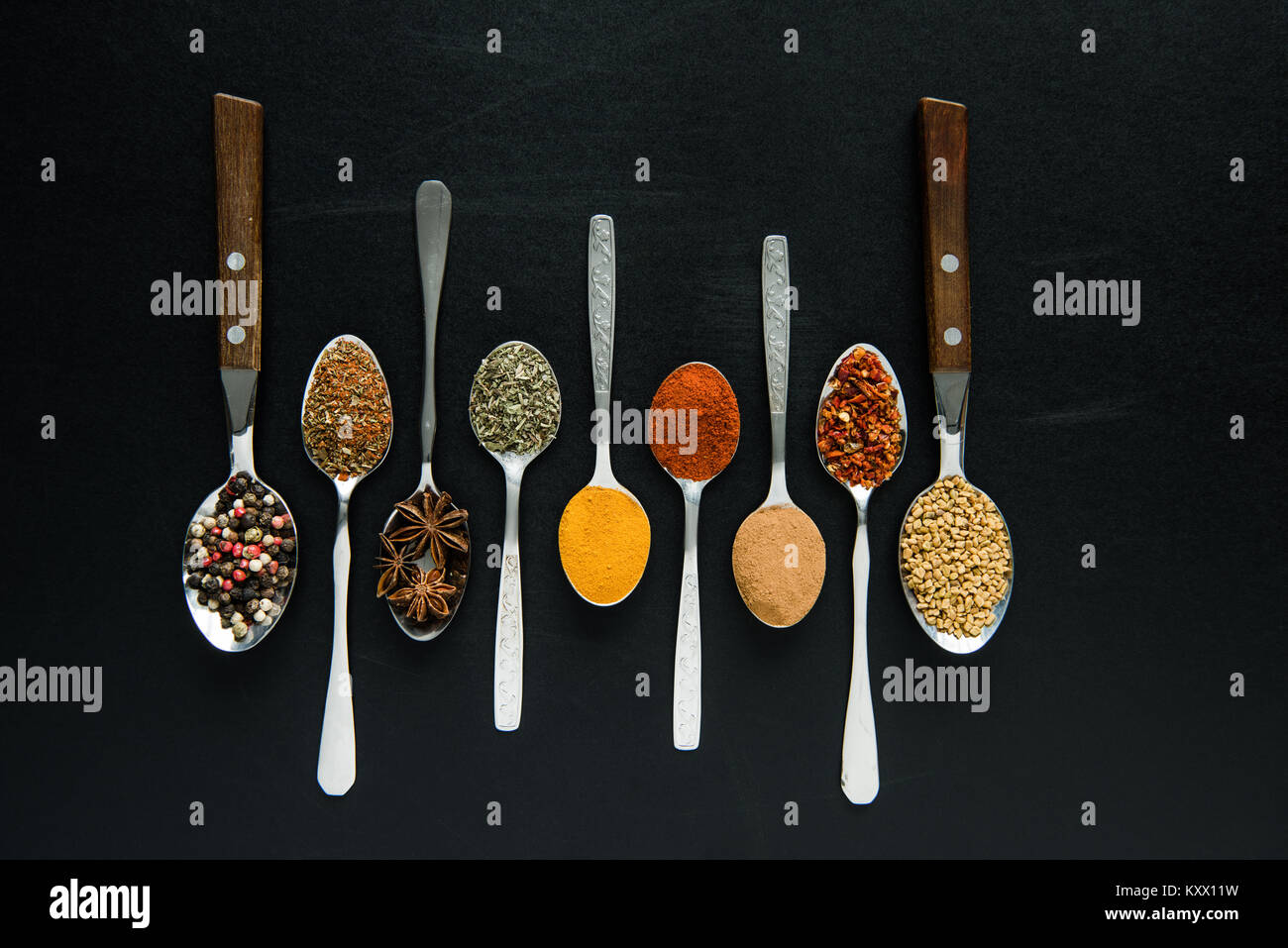 Vista superiore di varie spezie ed erbe in cucchiai di metallo isolato su nero Foto Stock