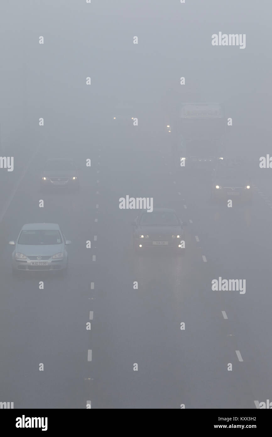 Autovetture e Veicoli alcuni con fari alcune luci spente guida su autostrada su di un nebbioso giorno nel Regno Unito Foto Stock