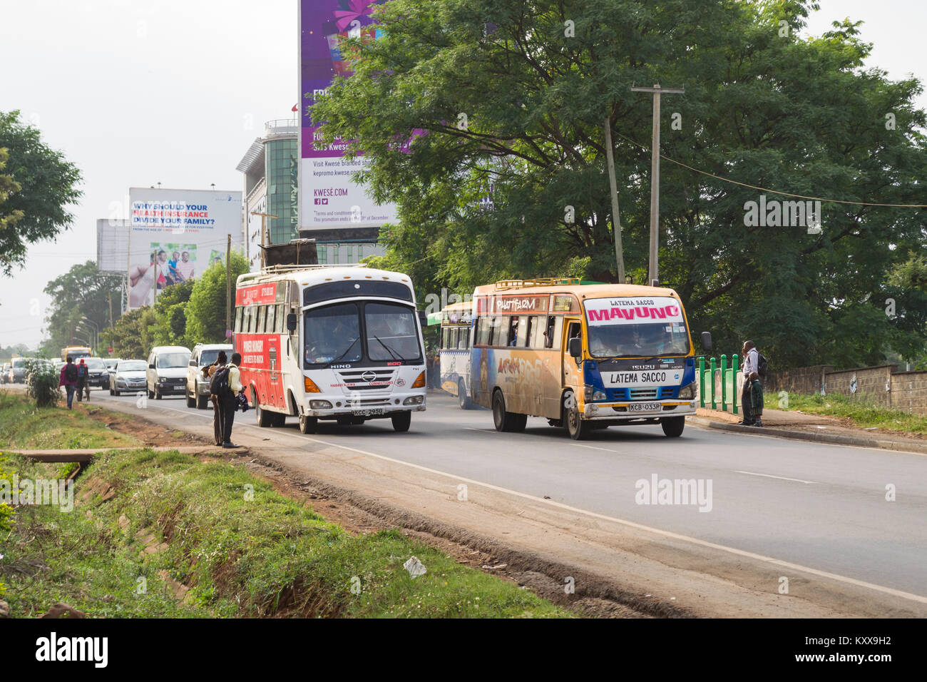 Autobus e altri veicoli auto giù Waiyaki via verso la città di Nairobi come pedoni attendere alla croce, Nairobi, Kenia Foto Stock
