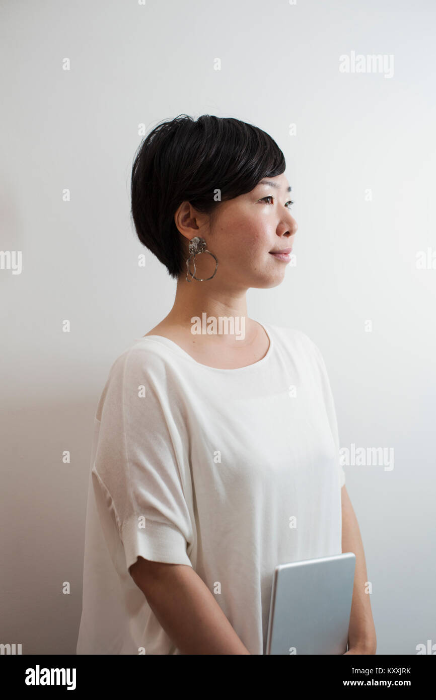 Vista di Profilo di donna con ordinamento capelli neri che indossa una camicia bianca in piedi in galleria d'arte. Foto Stock