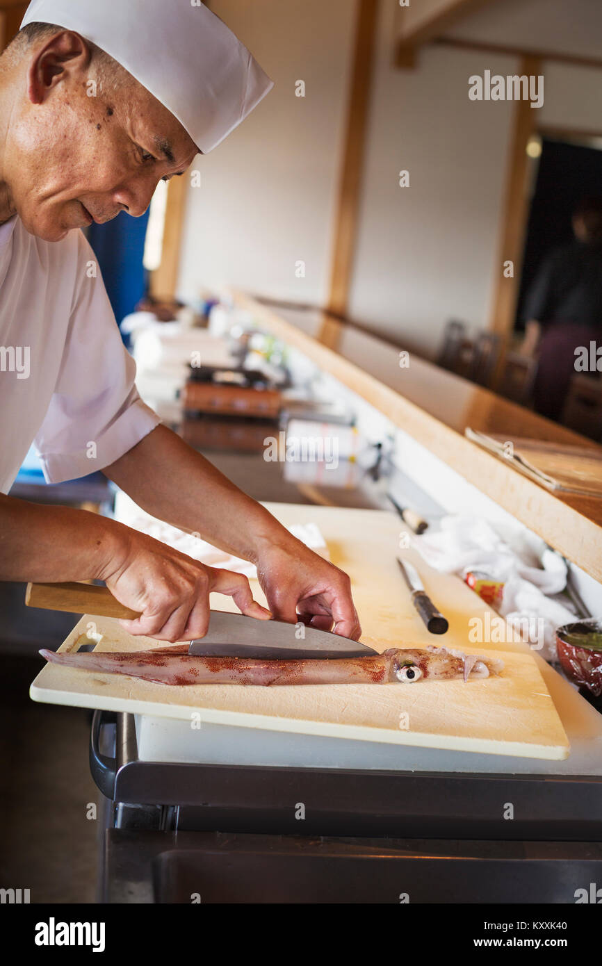Lo chef lavorano a un contatore a un I sushi giapponesi La cucina del ristorante, il taglio di un calamaro. Foto Stock