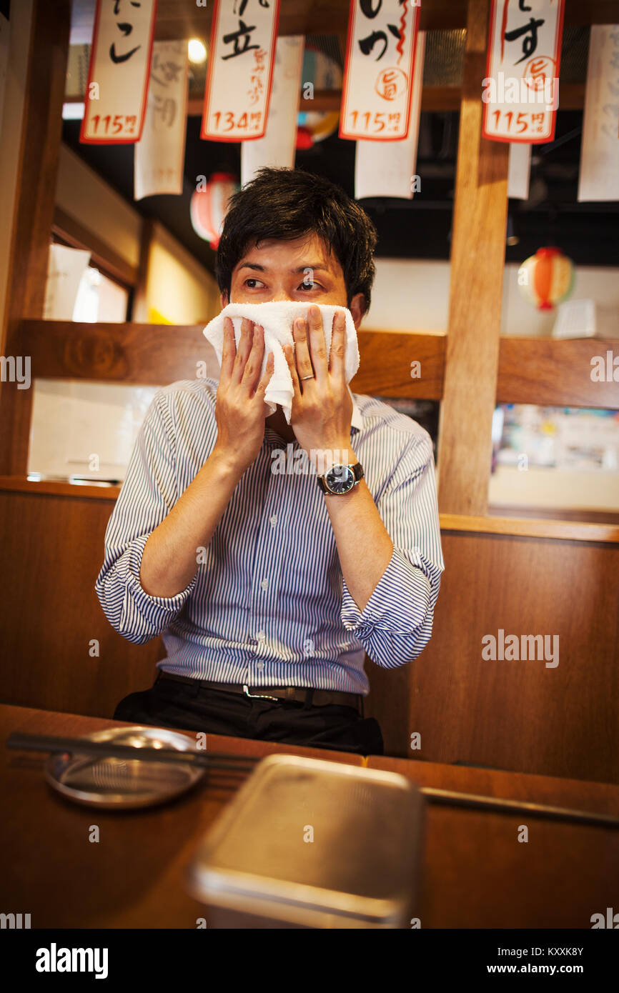 Uomo seduto a un tavolo in un ristorante, tergi il suo volto con il panno umido. Foto Stock