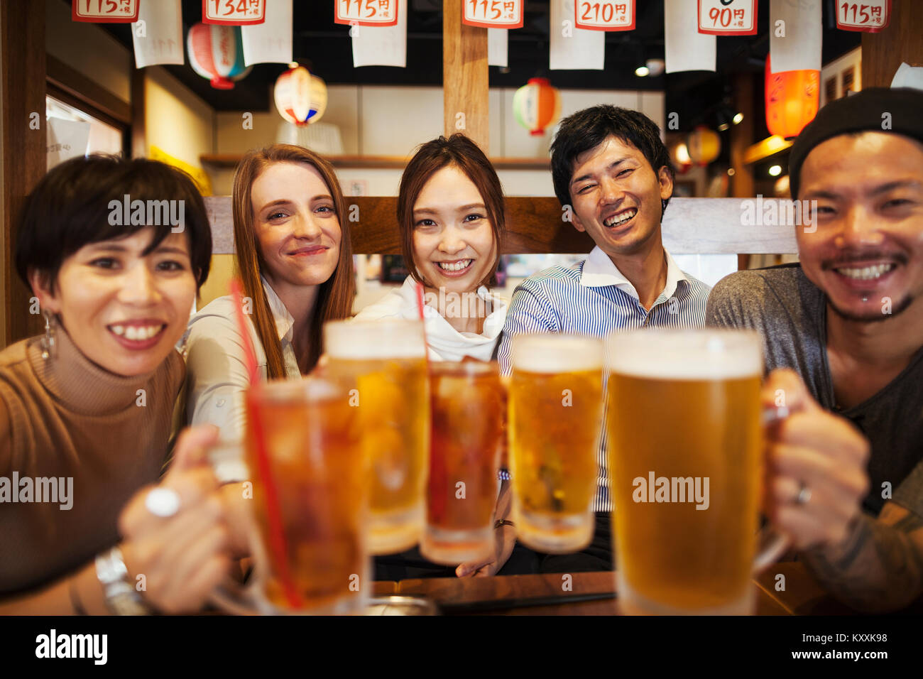 Cinque persone sidy seduta a fianco a un tavolo in un ristorante, tenendo grandi bicchieri di birra. Foto Stock