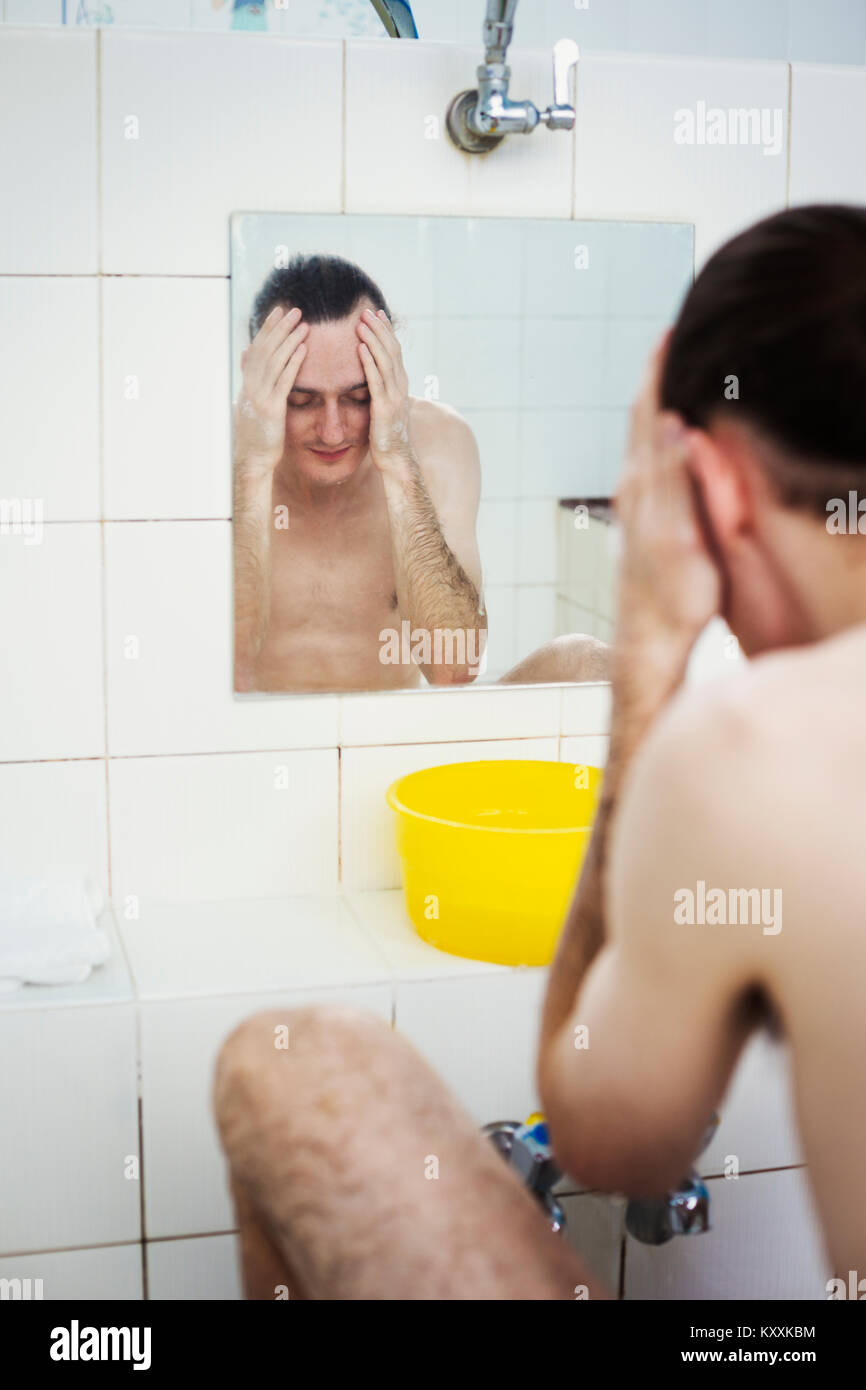 Un uomo lavando il suo volto in un capanno, vista in uno specchio. Foto Stock
