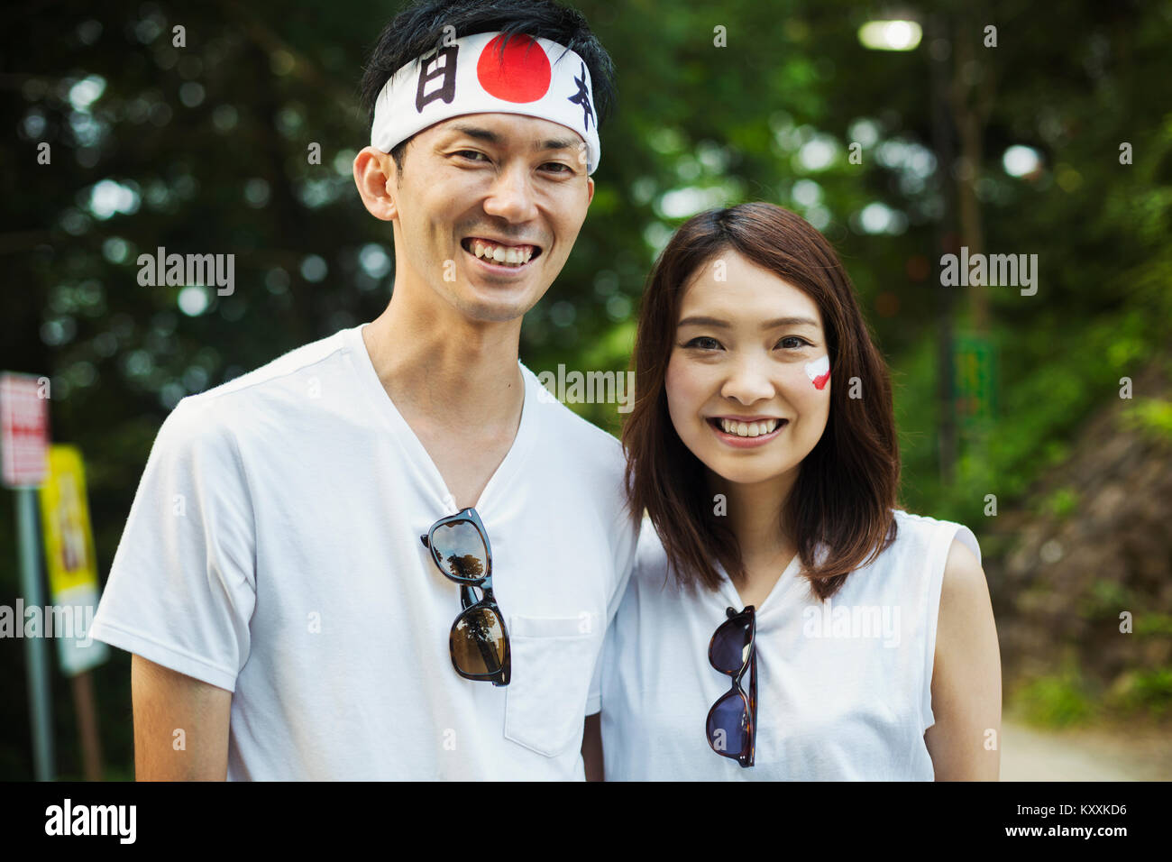 Ritratto di uomo che indossa la fascia e la giovane donna con capelli castani, bandiera giapponese dipinta sulla sua guancia, sorridente alla fotocamera. Foto Stock