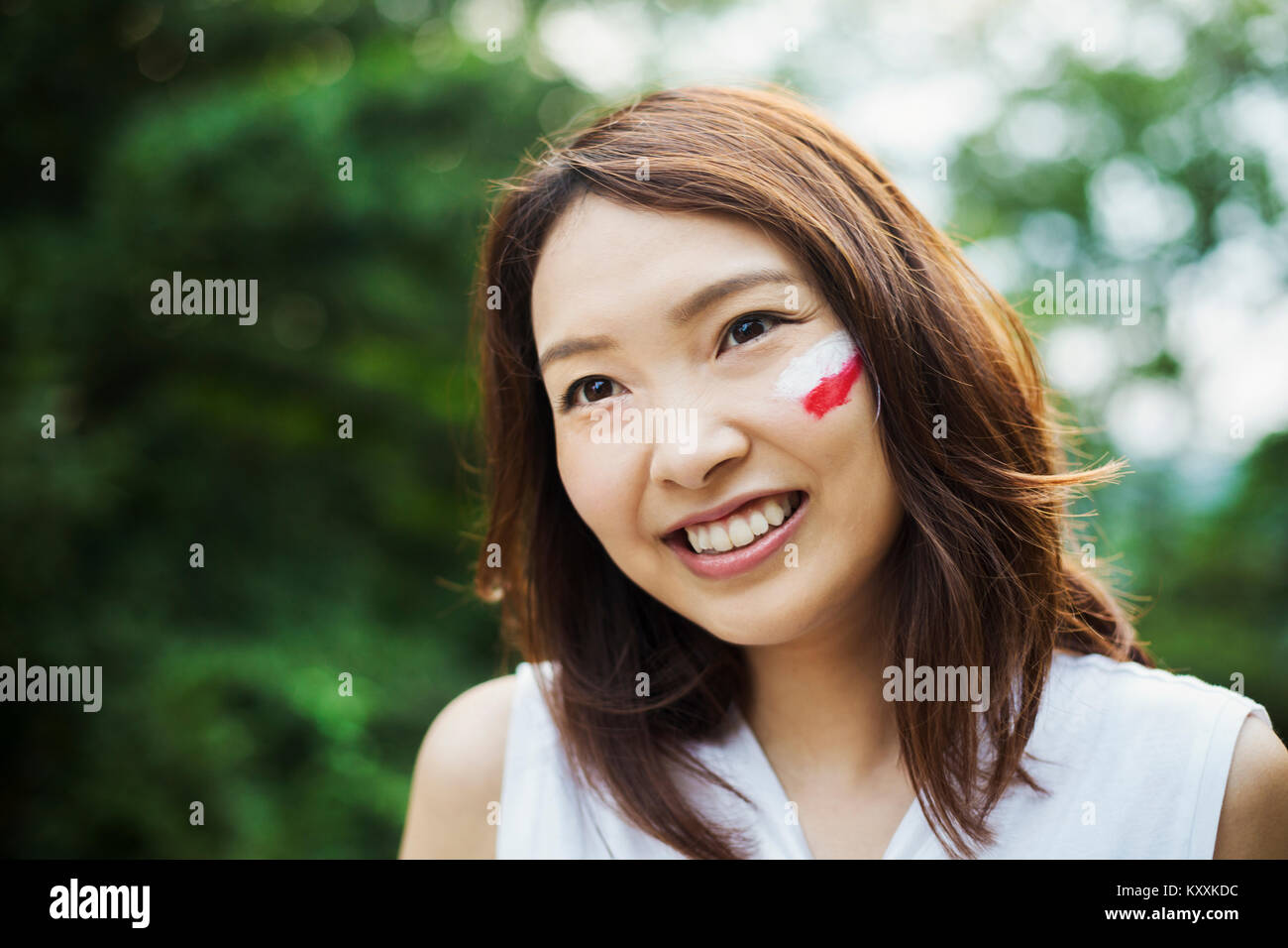 Ritratto di giovane donna con capelli castani, bandiera giapponese dipinta sulla sua guancia, sorridente alla fotocamera. Foto Stock