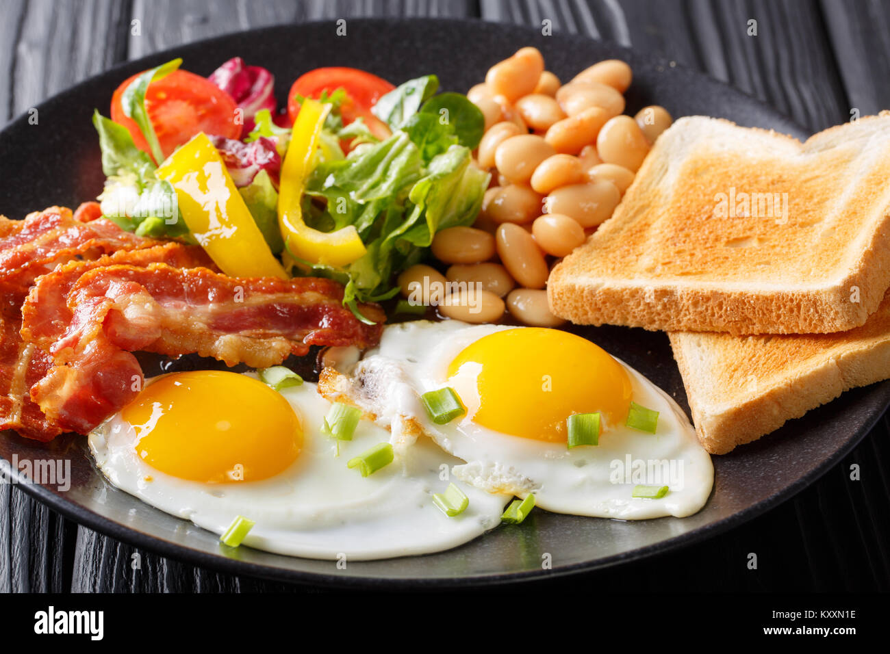 Deliziose uova fritte, pancetta, fagioli, toast e fresca insalata di verdure su una piastra sul tavolo orizzontale. Foto Stock