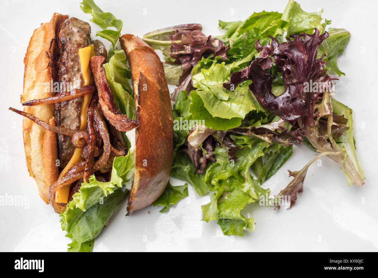 Splite hamburger con onios, pancetta, lattuga e formaggio placcato con un insalata verde su una piastra bianca Foto Stock