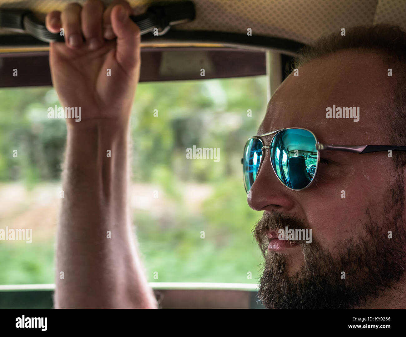 Colpo di Testa di uomo con occhiali da sole, equitazione in un auto, sudorazione e afferrando la maniglia di presa. Foto Stock