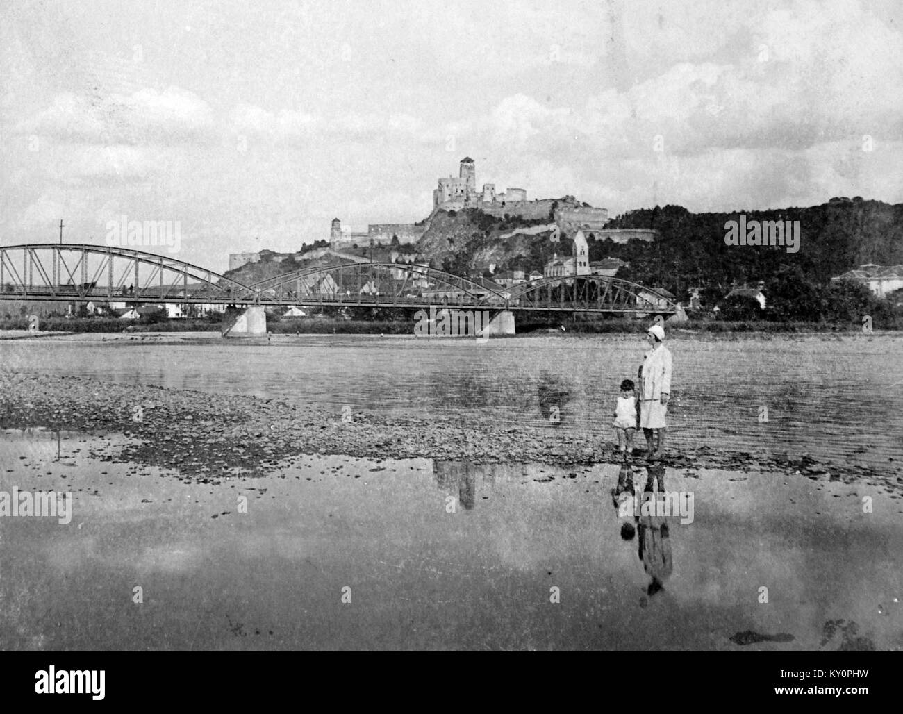 Questa immagine storica della collezione Fortepan raffigura un ponte sul fiume Vág, con un castello sullo sfondo. Mette in evidenza le infrastrutture e il paesaggio dell'Ungheria durante l'epoca. Foto Stock