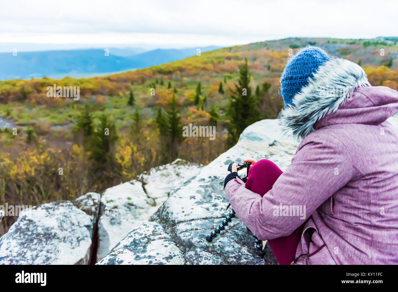 Udienza donna giovane fotografo con fotocamera e treppiede in autunno freddo mattino nella camicia cappotto, lana hat in orso rocce, West Virginia a scattare foto o Foto Stock