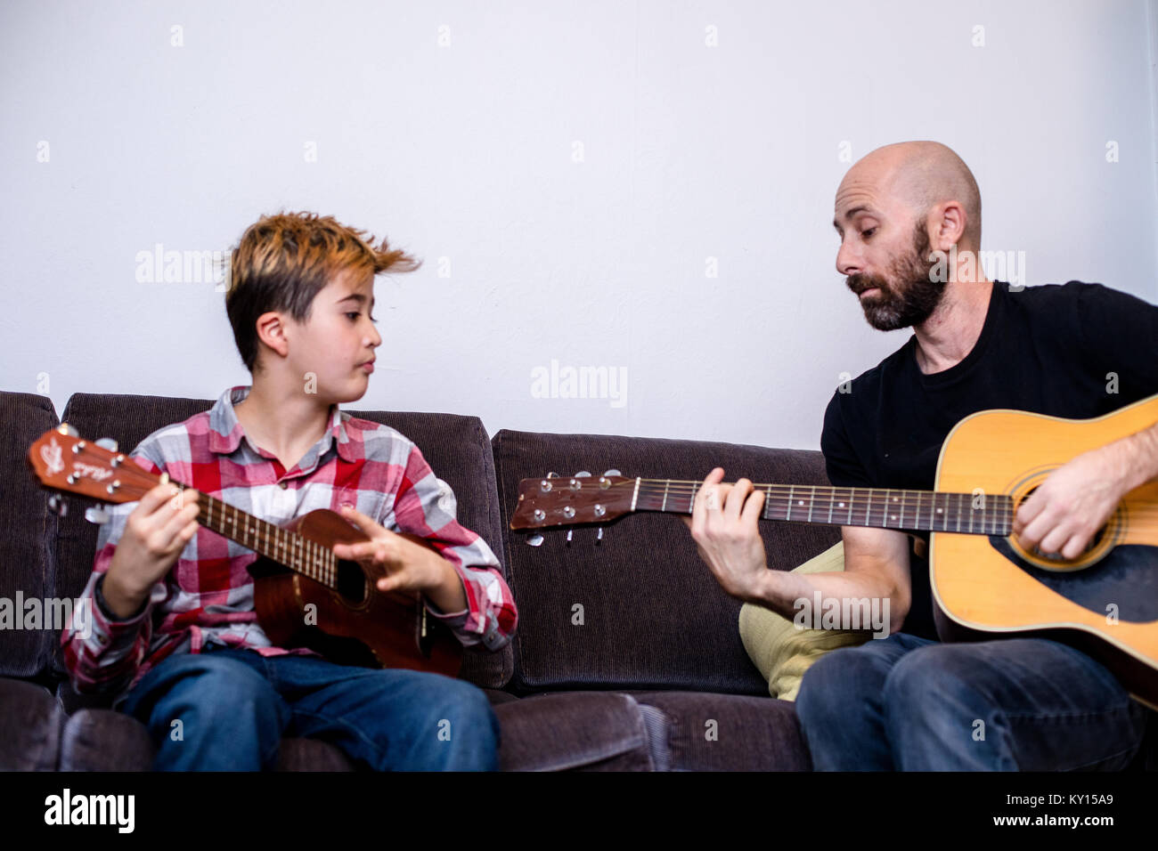 Undici anni ragazzo caucasico con la parte superiore della testa tinto arancio, indossando PLAID SHIRT, gioca mancino ukulele. Foto Stock