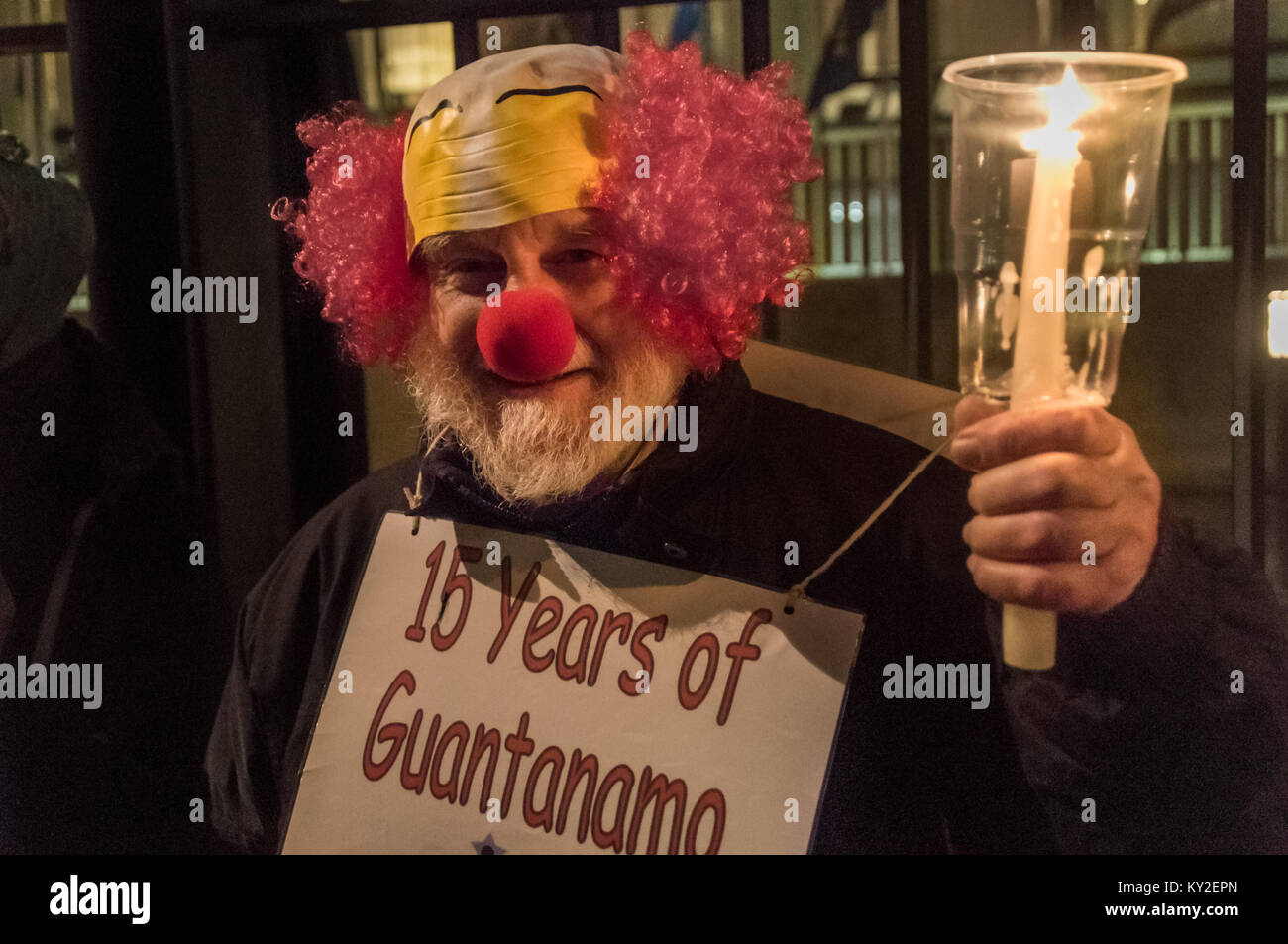 Londra, Regno Unito. Xi gen, 2018. Londra, Regno Unito. 11 gennaio 2018. Un manifestante indossa un clown maschera facciale e una targhetta "16 anni di Guantanamo non è ridere importa' alla fiaccolata outide l Ambasciata degli Stati Uniti ha segnato il Sedicesimo anniversario della tortura illegale camp a Guantánamo Bay dove 41 prigionieri sono ancora detenuti, soprattutto tenuto per un tempo indefinito senza carica o di prova e la maggior parte con lesioni permanenti dalla tortura che renderebbe la loro liberazione imbarazzante per il noi (e possibilmente UK) autorità. Manifestanti hanno acceso candele davanti all'ambasciata recinto compitazione 'GITMO' e poi si fermò portando candele accese Foto Stock