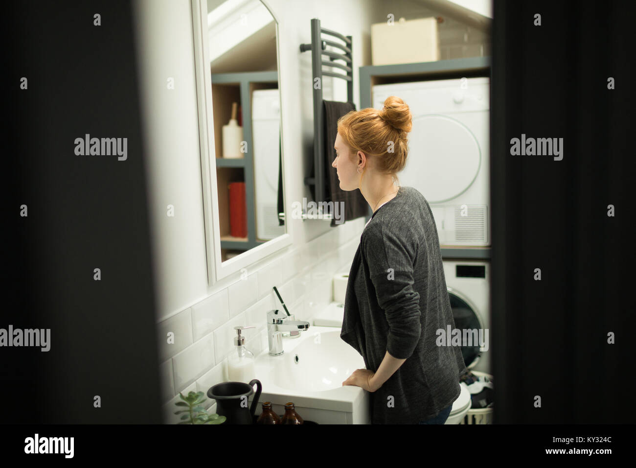 Giovane donna guardando nello specchio del bagno Foto Stock