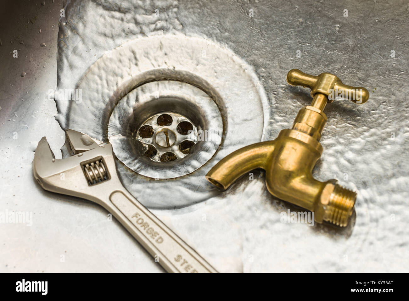 Una chiave inglese e il nuovo rubinetto appoggiata da un foro di scarico come acqua scorre verso il basso è Foto Stock